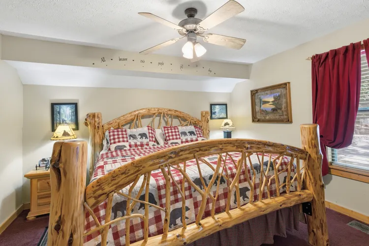 Bedroom with rustic log bed frame, red quilt, and ceiling fan.