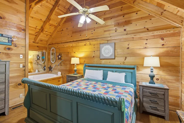 Bedroom with blue wooden bed frame, patterned quilt, and corner jetted tub.