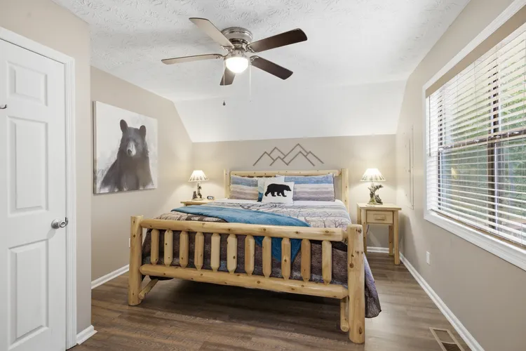 Bedroom with log bed frame, bear artwork, bedside tables, and a ceiling fan.