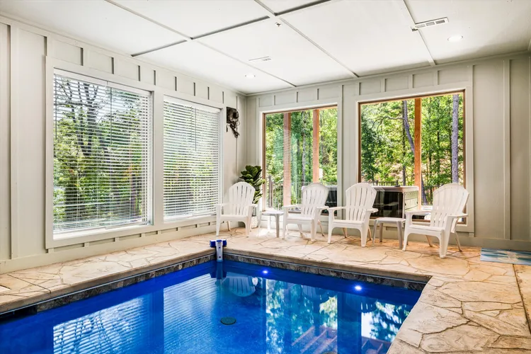 Indoor pool room with blue water, stone tile deck, and white chairs