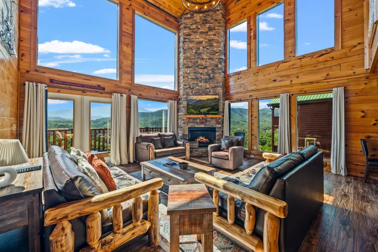 Two-story living room with stone fireplace, sofas, and large scenic windows.