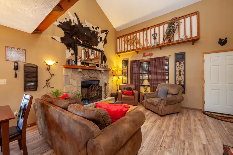 Living room with stone fireplace, brown sofas, and vaulted ceiling